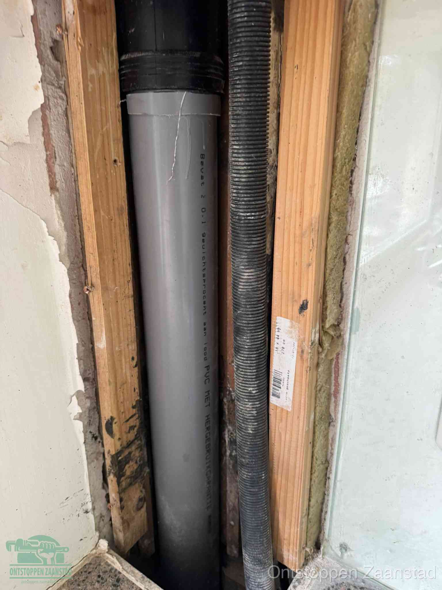 Een grijze PVC-afvoerbuis met een flexibele ribbelslang in een open wandconstructie, een verwaarloosde afvoer die te lang is blijven zitten in Zaanstad
