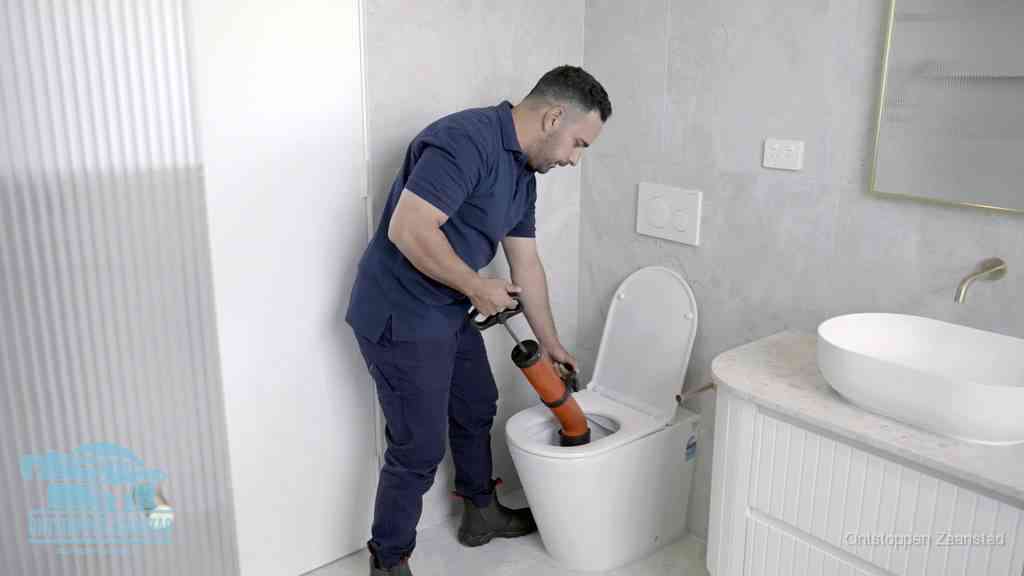 Een monteur buigt over een wandcloset en duwt met de hand een persluchtontstopper in de toiletpot om de verstopping handmatig los te maken in Zaanstad