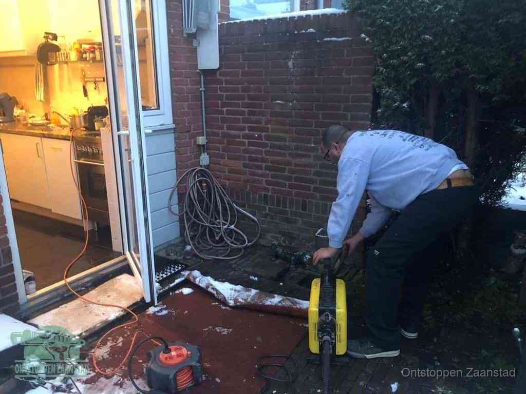 Een monteur werkt buiten bij een open riool-/grondput met een elektrische ontstoppingsmachine om een verborgen afvoerprobleem op te sporen in Zaanstad