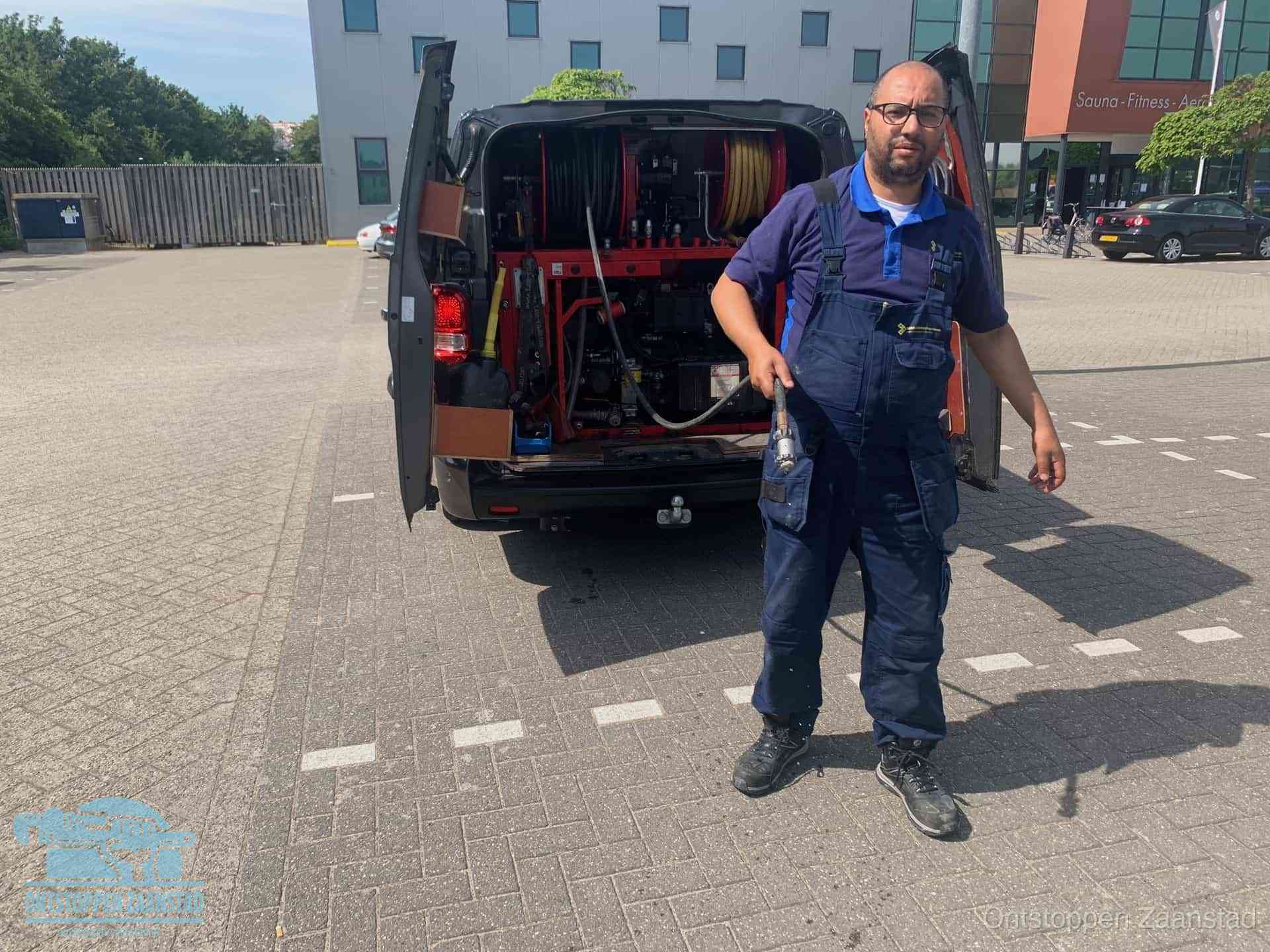 Een monteur bij zijn bestelbus met een hogedruk- en rioolreinigingsunit, klaar om de oorzaak van terugkerende wc-verstoppingen aan te pakken in Zaanstad
