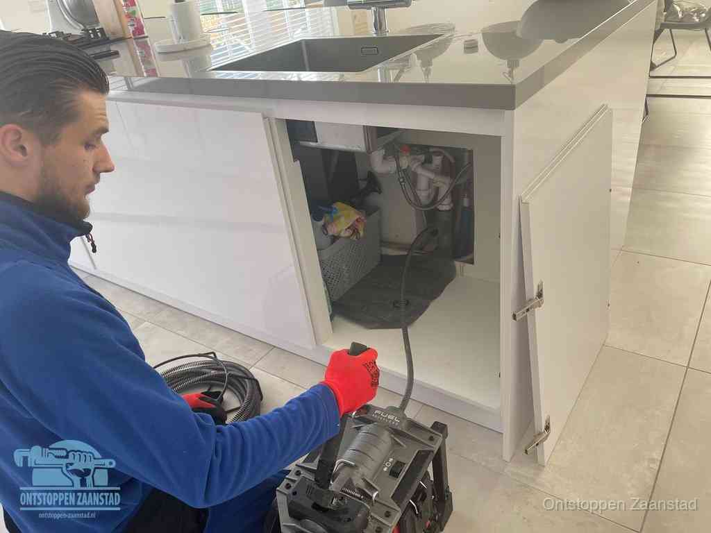 Monteur ontstopt met een veermachine een verstopte afvoer onder de gootsteen in Zaanstad