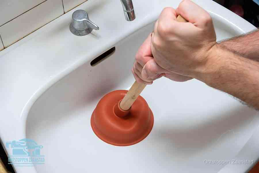 Twee handen gebruiken een rode rubberen plopper op een sanitair-afvoer om het toilet te ontstoppen in Zaanstad