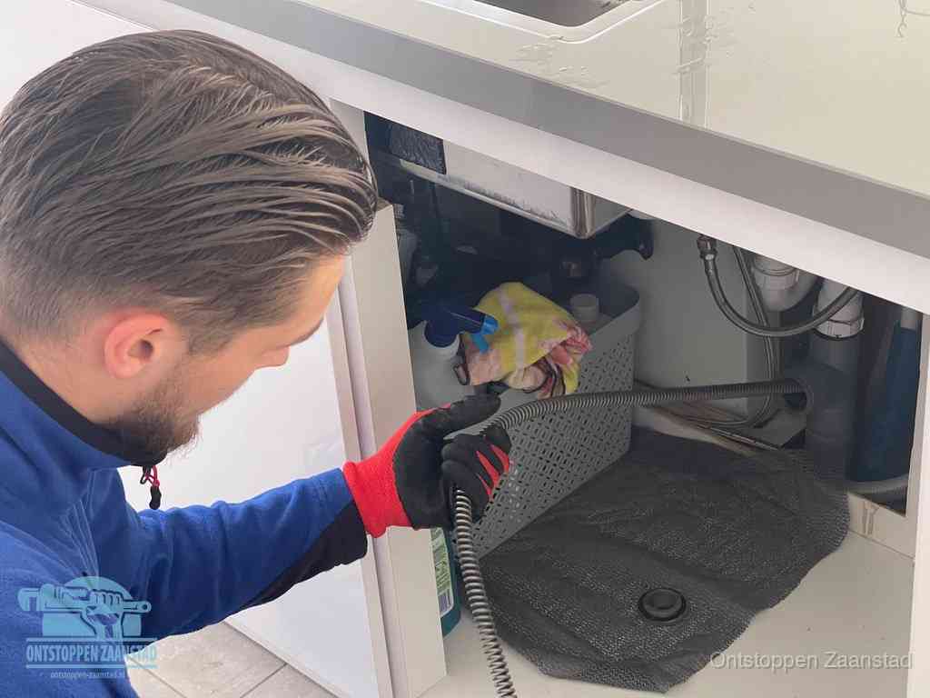 Een monteur voert een flexibele ontstoppingsveer in de afvoer om een verstopping voorbij de bocht van het toilet te bereiken in Zaanstad