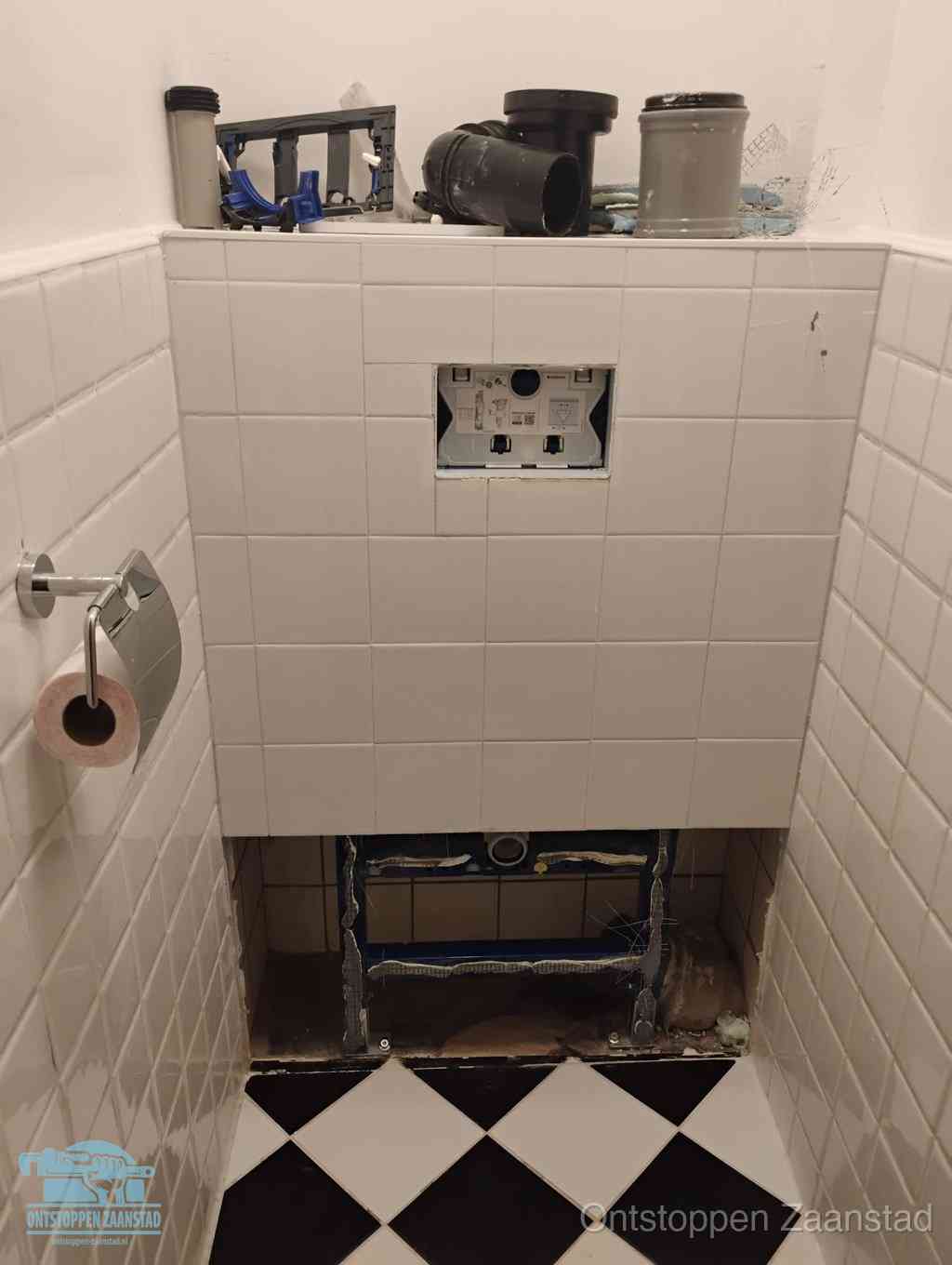 Een toiletruimte waar het hangtoilet en de inbouwreservoir-onderdelen zijn vrijgelegd voor onderhoud, periodiek nazicht voorkomt een wc-verstopping in Zaanstad