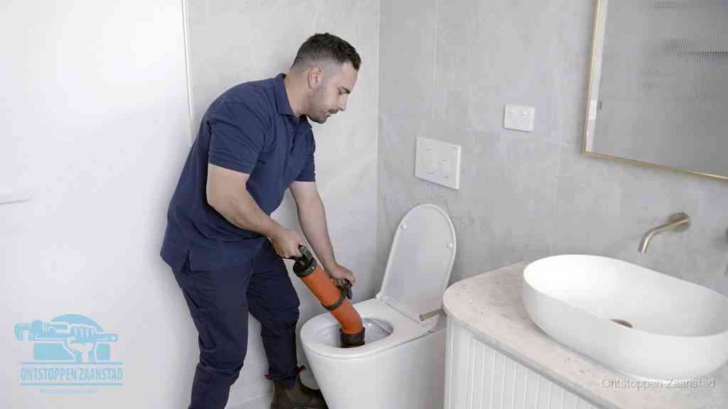 Een man gebruikt een handmatige luchtdruk-ontstopper in een modern betegeld toilet om zelf de wc te ontstoppen in Zaanstad